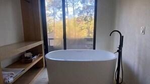 Une salle de bain dotée d’une grande baignoire, d’une douche et offrant une vue sur les arbres grâce à une porte coulissante.