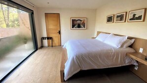 Une chambre moderne avec un grand lit, un plancher en bois, une porte-fenêtre coulissante et des tableaux encadrés accrochés au mur.