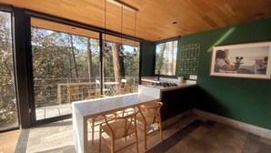 A modern kitchen with a large island, wooden chairs, and a view of the forest through large windows. - Cabaña Oyamel en Valle de Bravo (Valle de Bravo)