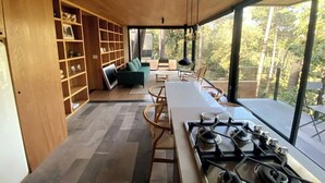 A modern kitchen with a gas stove, wooden shelves, and a dining area with a table and chairs. - Cabaña Oyamel en Valle de Bravo (Valle de Bravo)