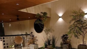 Ein modernes Interieur mit Holzbalkendecke, eingelassener Beleuchtung und verschiedenen topfgepflanzten Pflanzen auf einem gefliesten Boden.