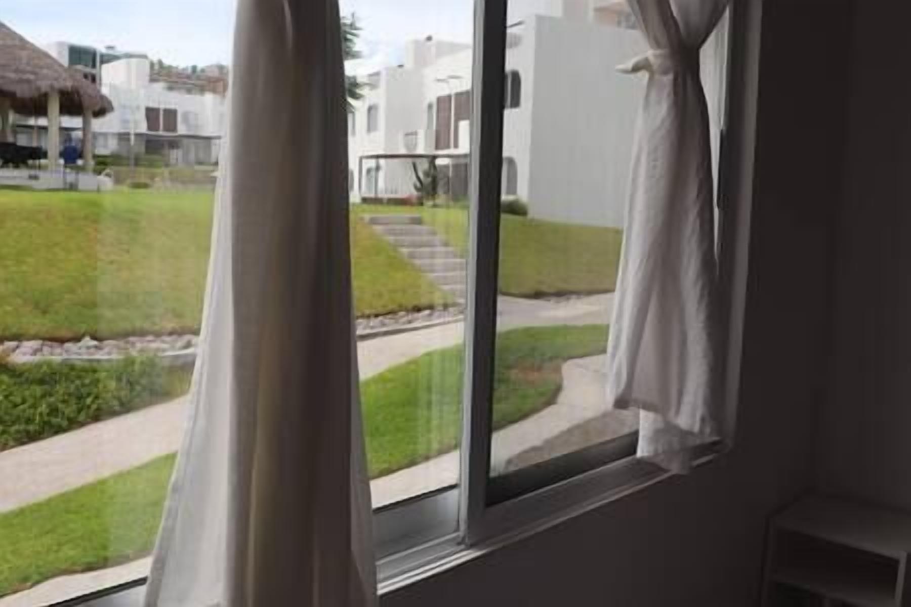 A view from a window with curtains, overlooking a well-maintained lawn and a pathway leading to a building.