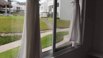 A view from a window with curtains, overlooking a well-maintained lawn and a pathway leading to a building.