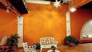 An indoor patio area with white metal chairs and a small table, surrounded by orange walls and potted plants.