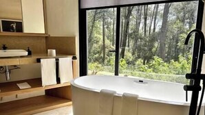 A modern bathroom with a freestanding bathtub, a sink, and a window with a forest view. - Suite Cedro, Cabaña Boutique en Valle de Bravo (Valle de Bravo)