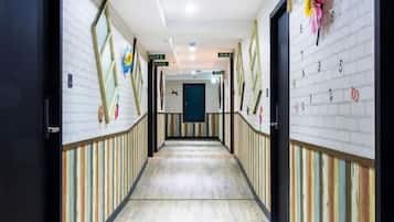 Corredor de hotel com paredes listradas, piso de madeira e uma porta azul no final.