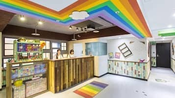 Espaço de recreação infantil com teto em arco-íris, mesa de brincar e balcão de recepção.