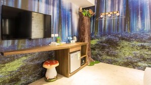 A room with a TV mounted on the wall, a wooden desk with a small fridge, and a forest-themed mural. - RF Hotel - Sanchong (New Taipei City)