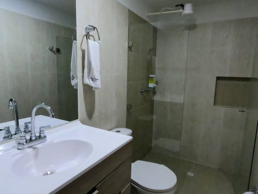 A bathroom with a sink, mirror, toilet, and shower area.
