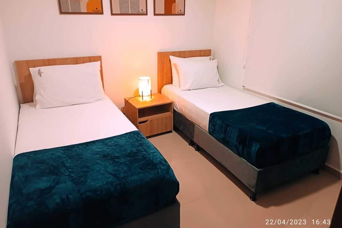 A twin room with two single beds, a nightstand, and a wall-mounted lamp.