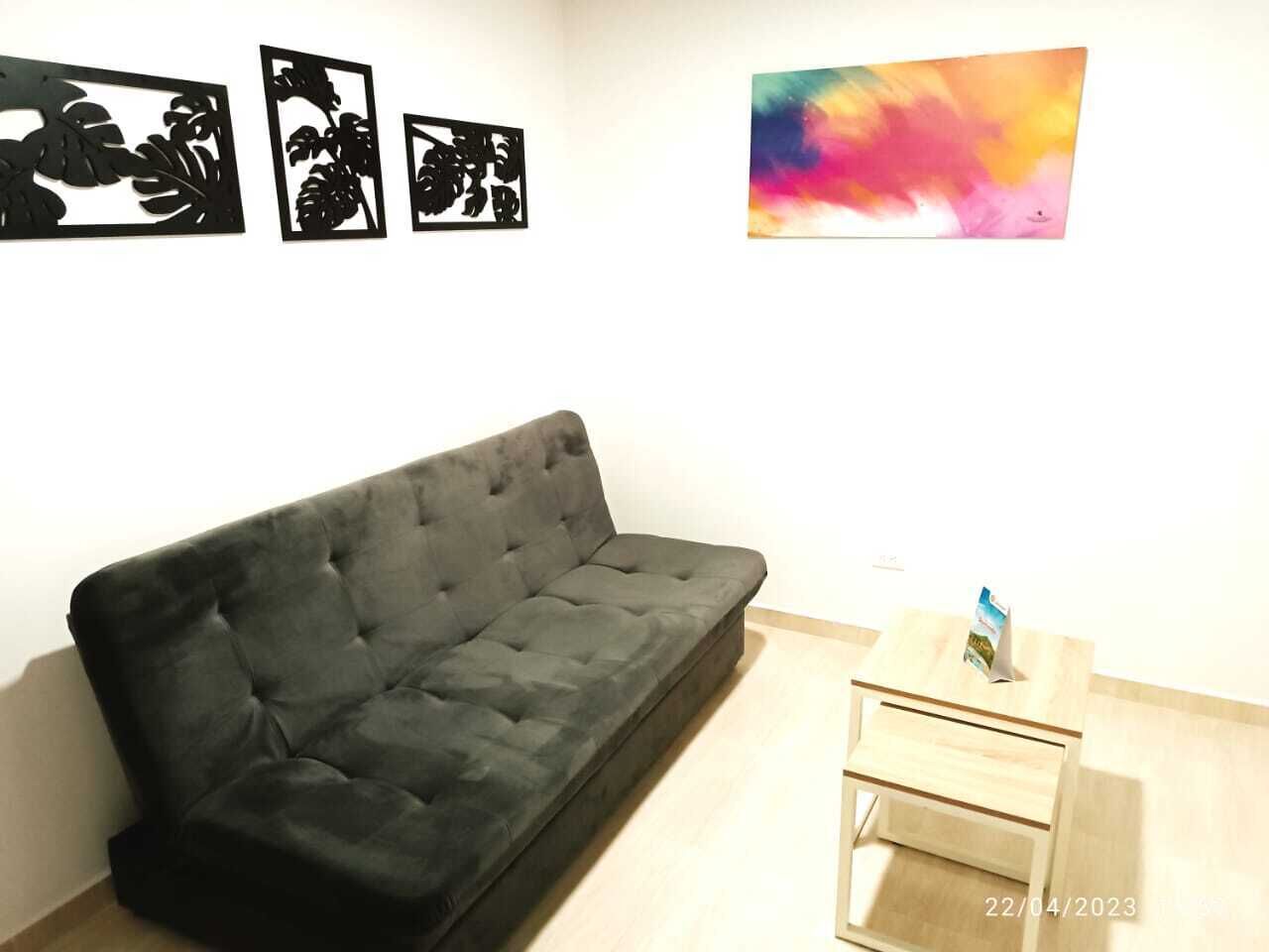 A room with a black sofa, a small wooden table with a magazine, and three black artwork pieces on the wall.