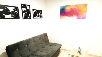 A room with a black sofa, a small wooden table with a magazine, and three black artwork pieces on the wall.