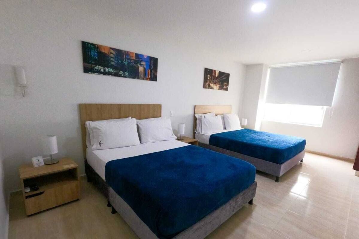 A hotel room with two beds, a nightstand, and a window with blinds.