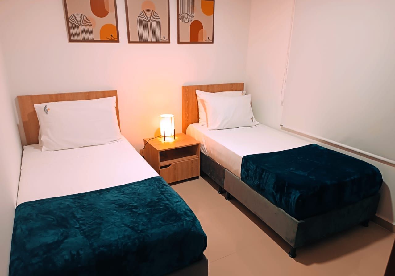 Habitación doble con dos camas individuales, una mesita de noche y una lámpara de pared.
