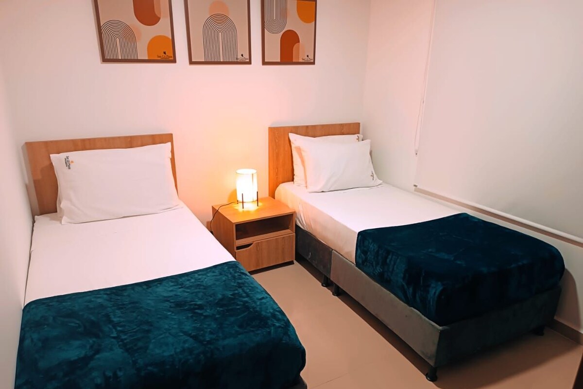Habitación doble con dos camas individuales, una mesita de noche y una lámpara de pared.