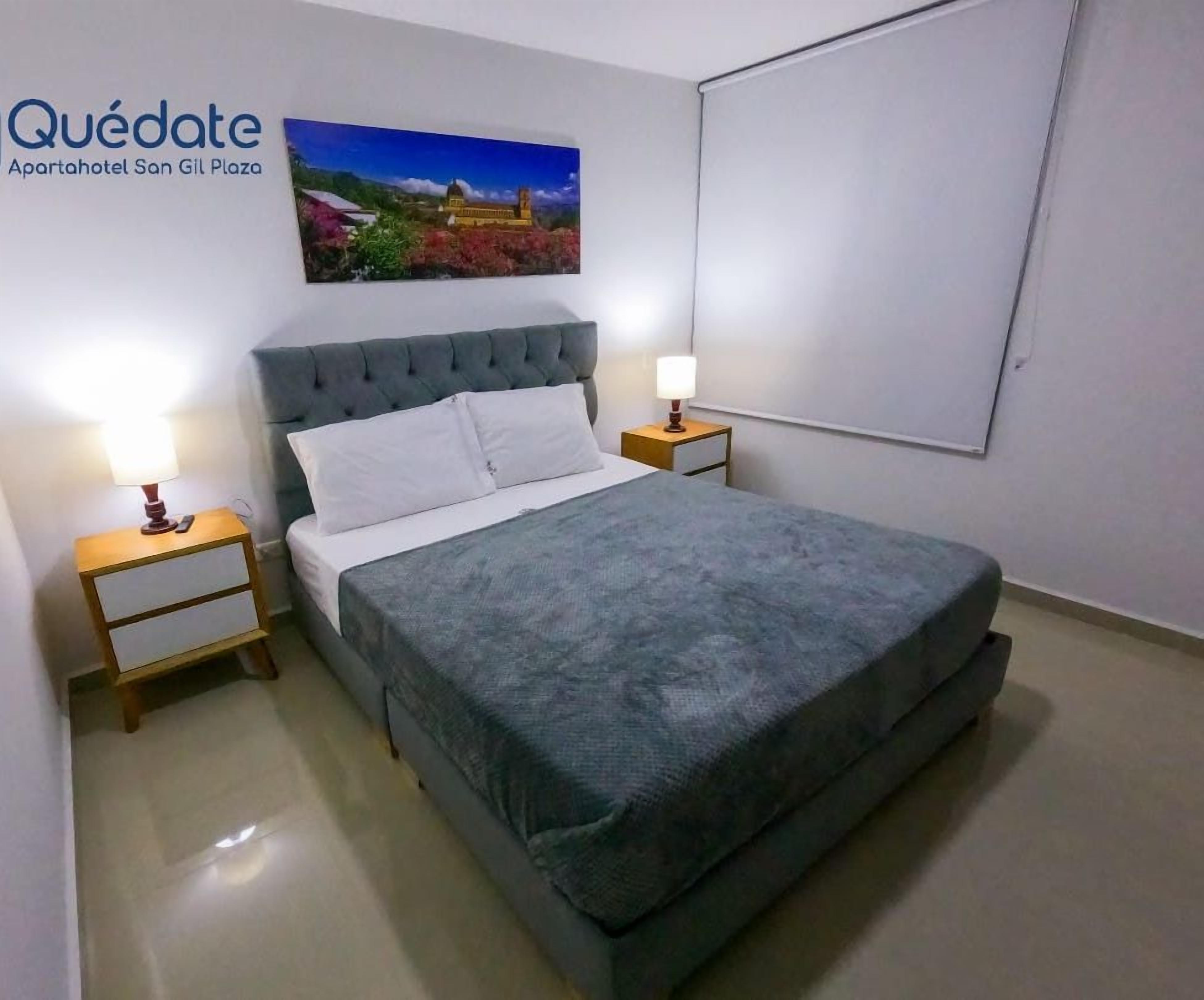 A bedroom with a large bed, two bedside tables, a nightstand, a wall-mounted TV, and a painting of a landscape.