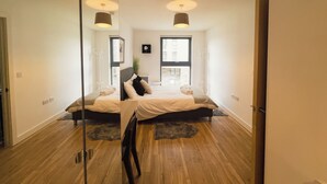Une chambre moderne avec un grand lit, deux tables de chevet, un miroir et une vue sur la ville grâce à une grande fenêtre.