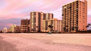 A beachfront hotel with high-rise buildings, a sandy beach, and a sunset sky. - Island Escape - Waterfront pool home! Walk to the beach! (Marco Island)