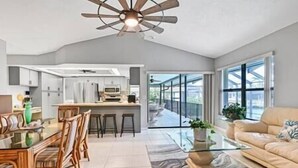 A modern kitchen with white cabinets, a dining area with wooden chairs, a glass coffee table, and a large window with a view of the outside. - Island Escape - Waterfront pool home! Walk to the beach! (Marco Island)