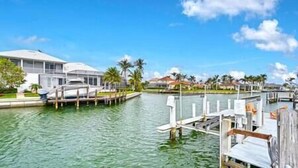 A marina with docked boats, a clear blue sky, and residential buildings in the background. - Island Escape - Waterfront pool home! Walk to the beach! (Marco Island)