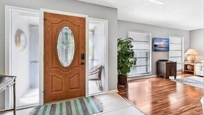 A spacious living room with a wooden door, a large potted plant, and a view of the outside. - Island Escape - Waterfront pool home! Walk to the beach! (Marco Island)