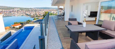 A balcony with a pool, outdoor furniture, and a view of a town and lake.