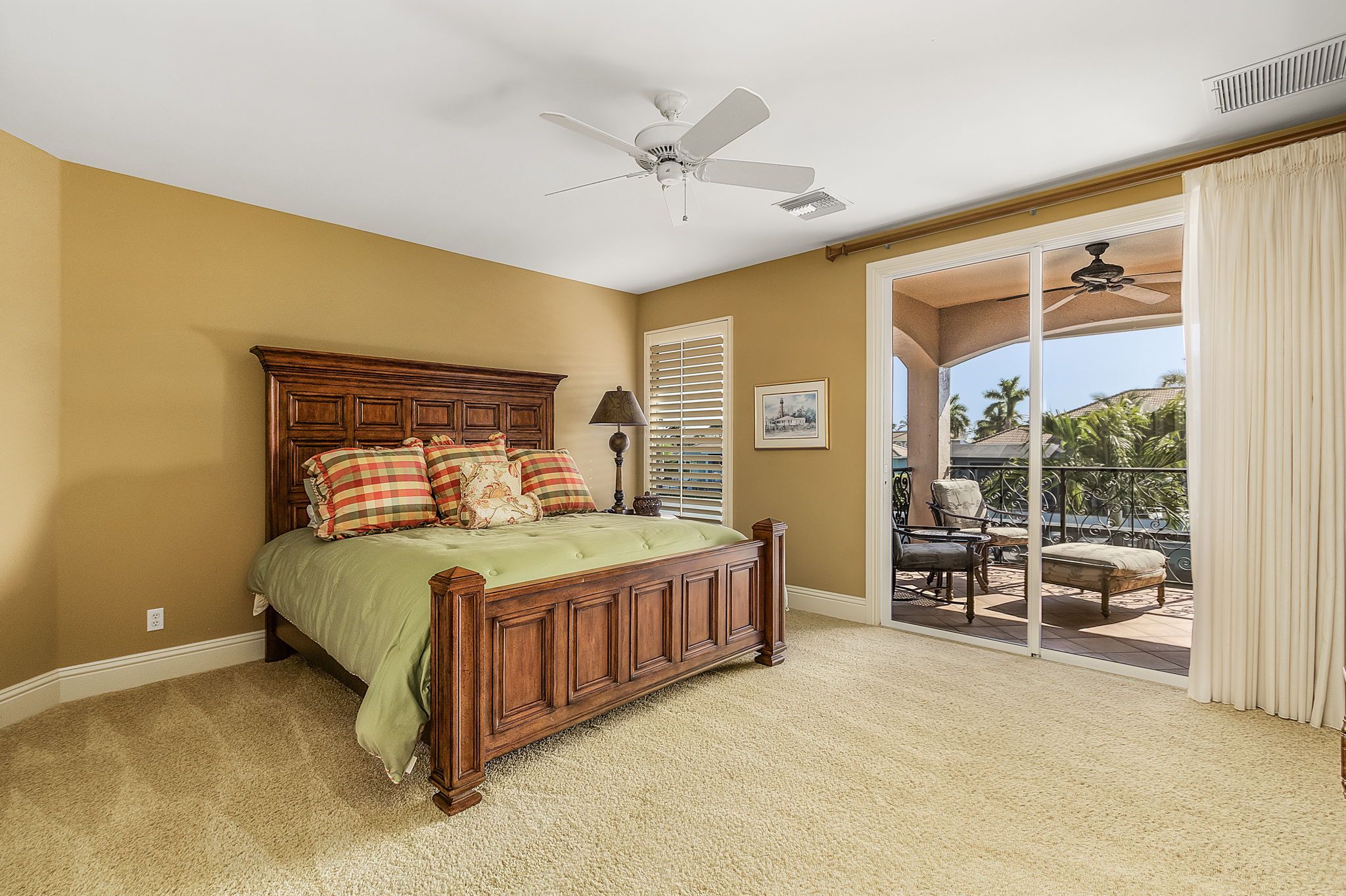A bedroom with a large bed, a ceiling fan, and a view of an outdoor patio with furniture.