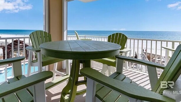 Un balcon avec une table ronde et des chaises vertes, donnant sur une plage sous un ciel dégagé.