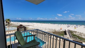 Un balcon avec vue sur une plage, une piscine et un poste de surveillance des sauveteurs.