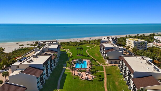 Ein Resort mit mehreren Gebäuden, einem zentralen Poolbereich und Blick auf den Strand.