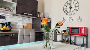 A modern kitchen with a dining table, a vase with roses, a clock, and a red microwave.