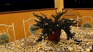 Un balcon agrémenté d’une nappe à motifs, d’une plante en pot et de guirlandes lumineuses, avec une chaîne de montagnes en toile de fond.