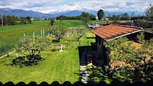 Une maison de campagne avec un toit recouvert de tuiles rouges, entourée de champs verdoyants et d’arbres.