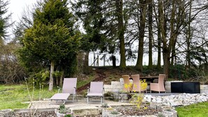 Een tuin met buitenmeubels, stenen plantenbakken en een achtergrond van bomen.