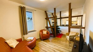 Een woonkamer met een houten vloer, een rode leren bank, een raam met houten kader, een kleine kerstboom en een televisie op een houten dressoir.