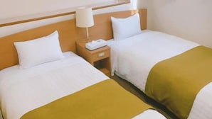 A hotel room with two beds, a nightstand, a lamp, and a window with curtains.