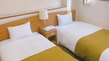 Een hotelkamer met twee bedden, een nachtkastje, een lamp en een raam met gordijnen.