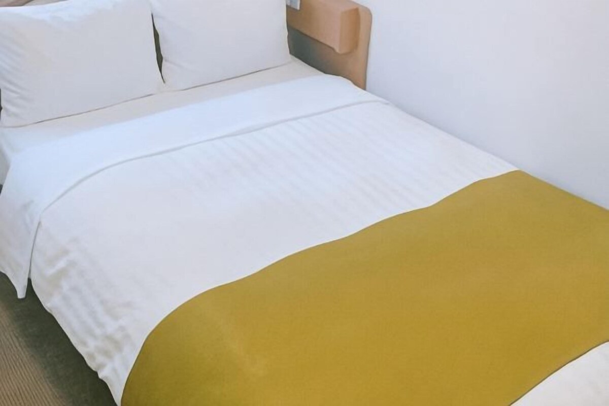 A bed with a white duvet and a mustard-colored blanket.