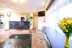 A hotel reception area with a reception desk, a potted plant, and a vase of flowers. - Urban Hotel Tokyo Fuchu East Exit (Fuchu)