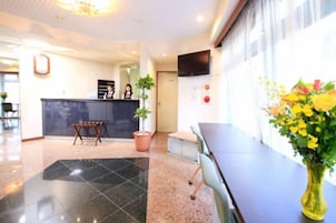 A hotel reception area with a reception desk, a potted plant, and a vase of flowers.