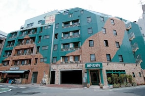 A multi-story building with a green facade and a ground-level entrance. - Urban Hotel Tokyo Fuchu East Exit (Fuchu)