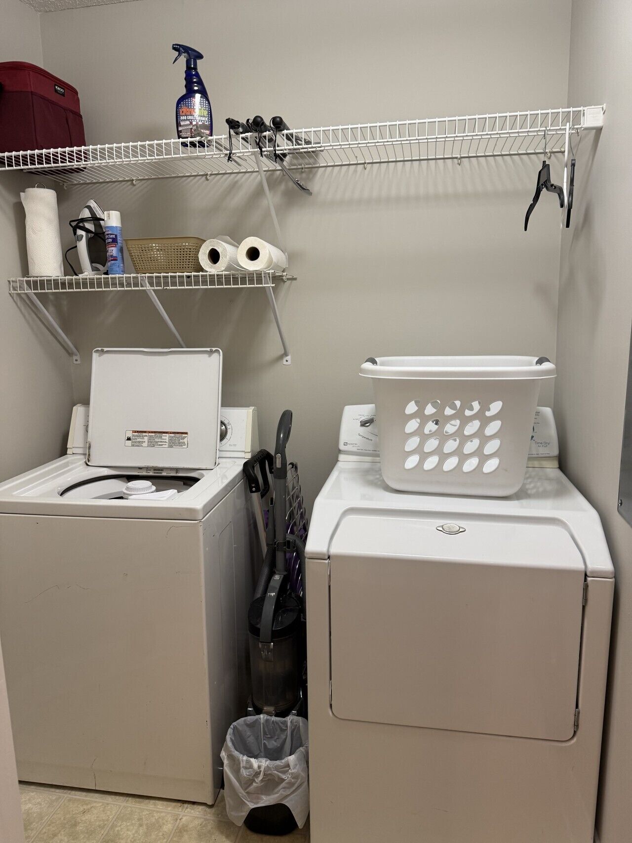 A laundry area with a washing machine, dryer, and shelves with laundry supplies.