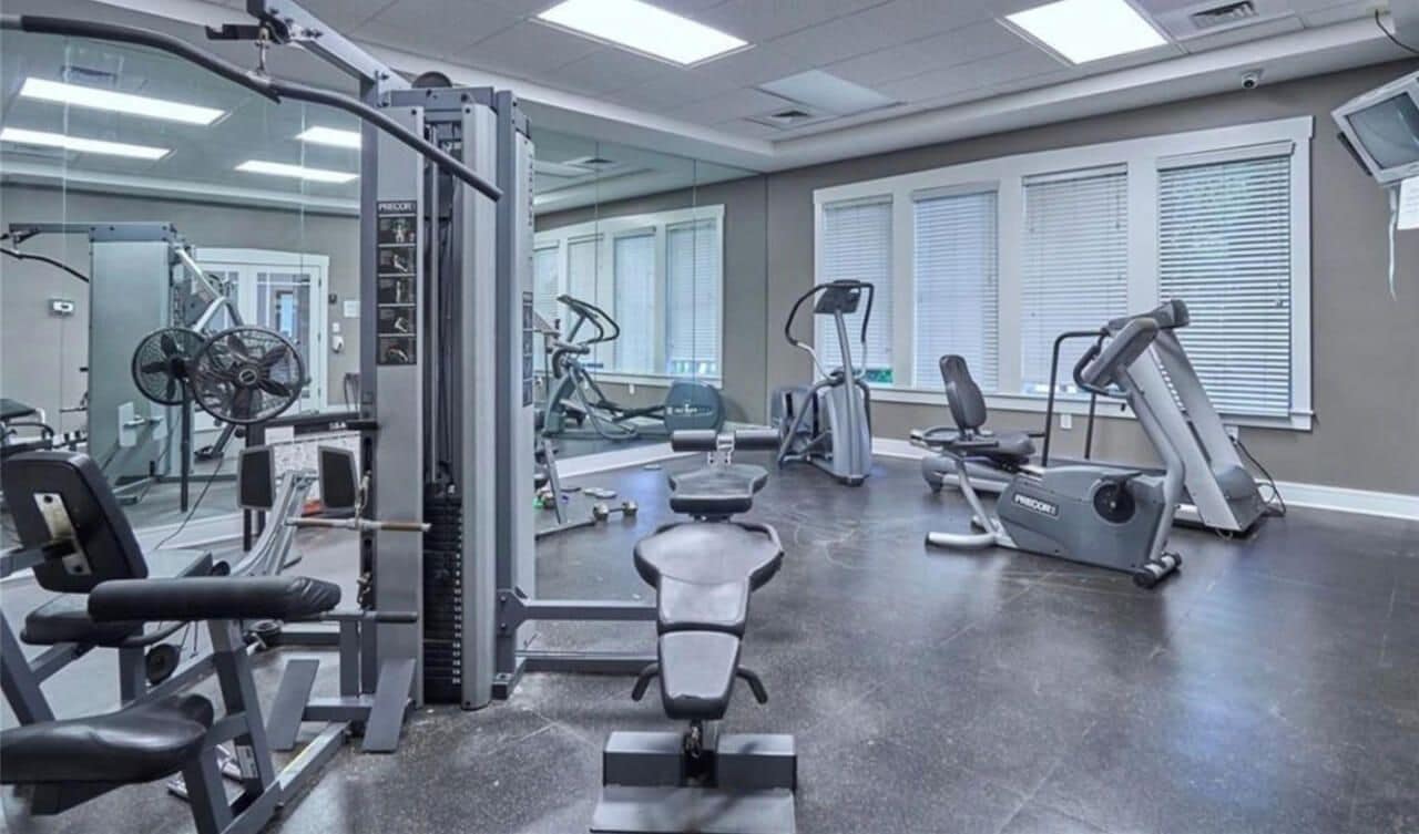 A gym with various exercise equipment, including treadmills, weight machines, and a bench.