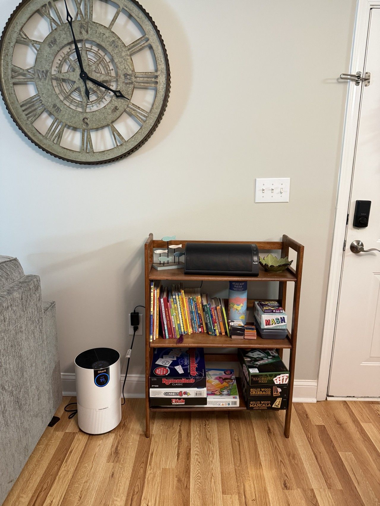 A room with a wooden bookshelf, a wall clock, and a white device on the floor.