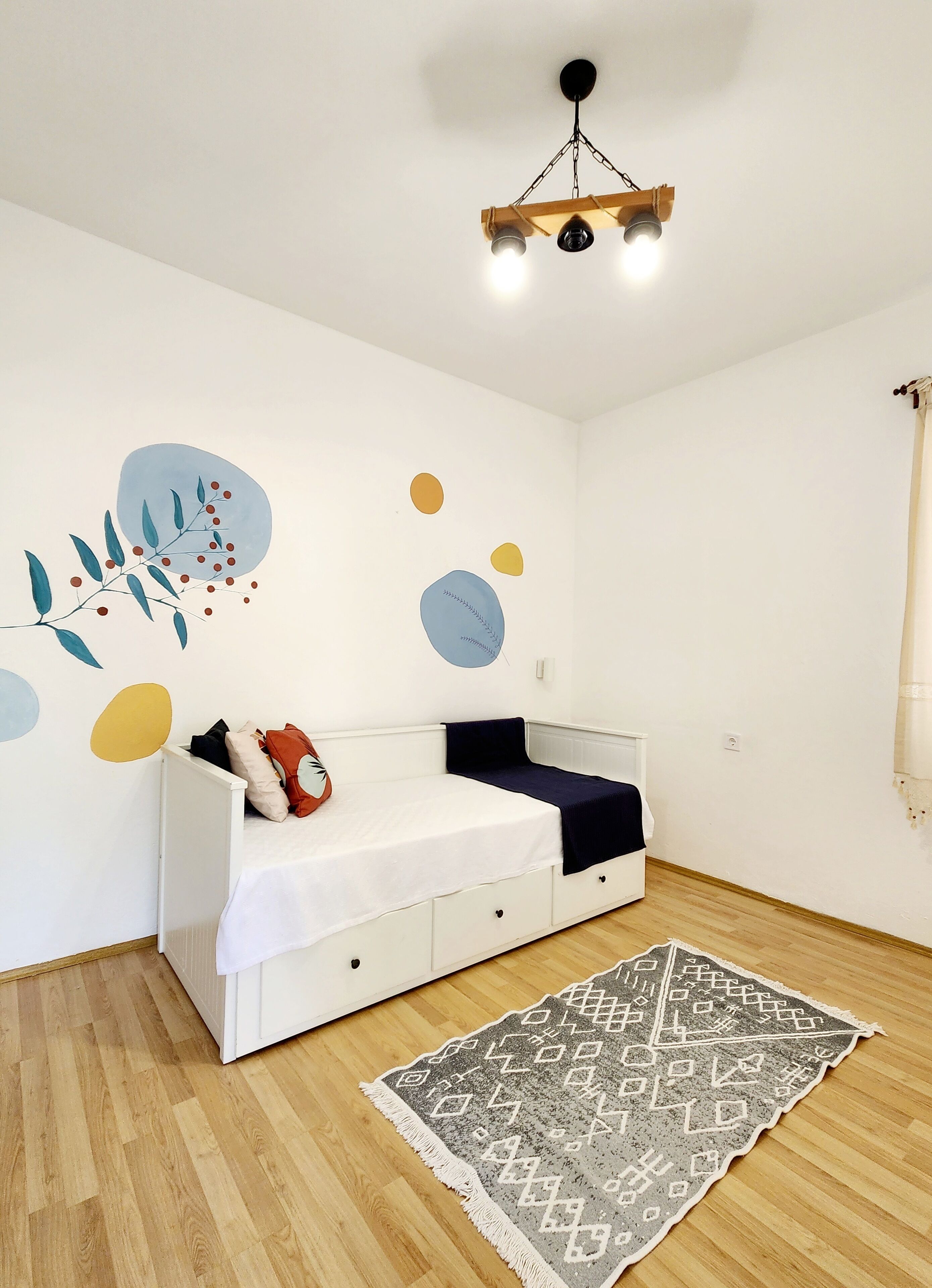 Una habitación con cama blanca, suelo de madera, alfombra estampada y cuadros abstractos en la pared.