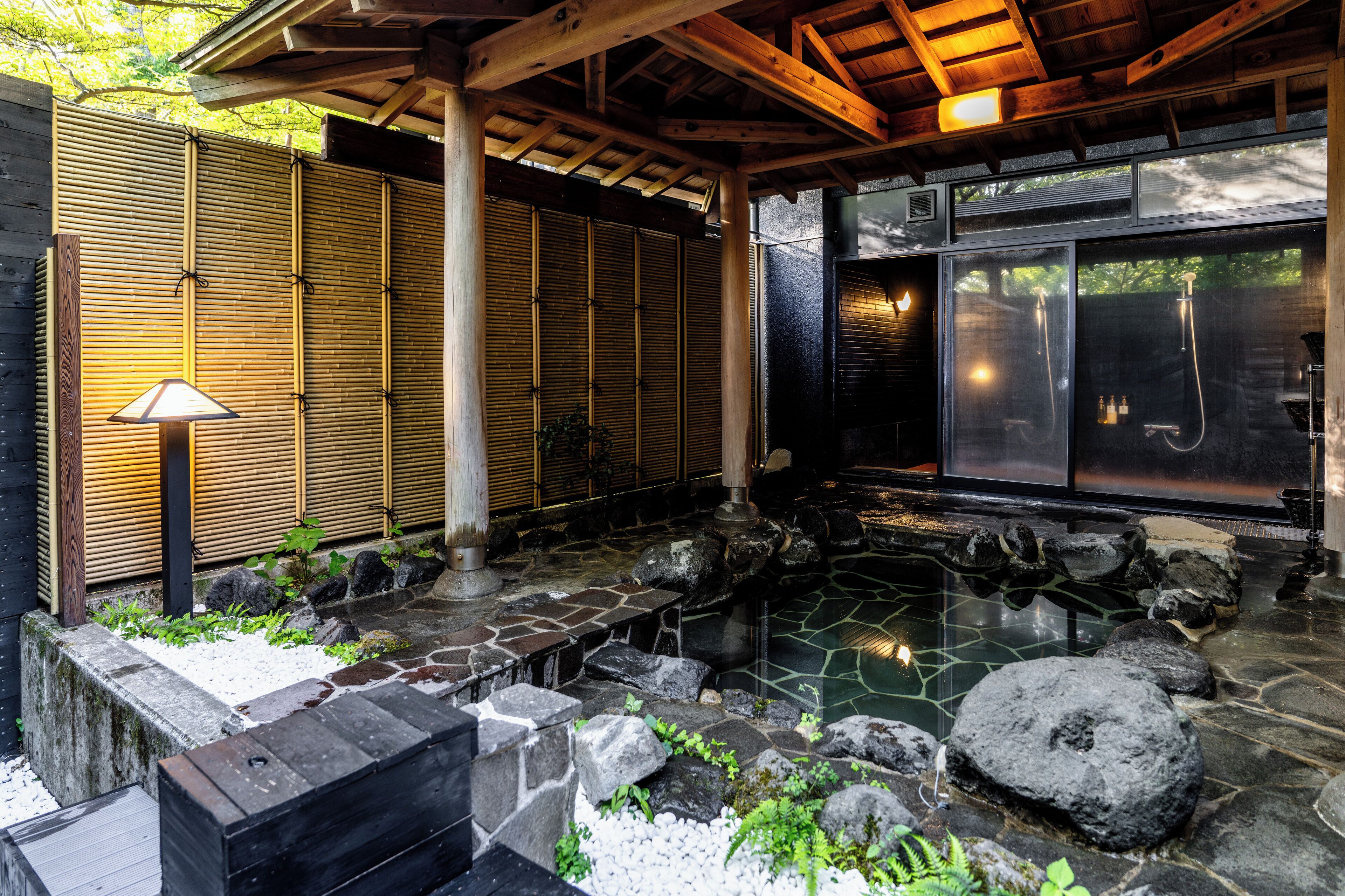 Un jardín japonés tradicional con un estanque de piedra, paredes de bambú y una pérgola de madera.
