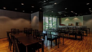 Un salón de conferencias con varias mesas y sillas, amplias ventanas y un diseño moderno en el techo.