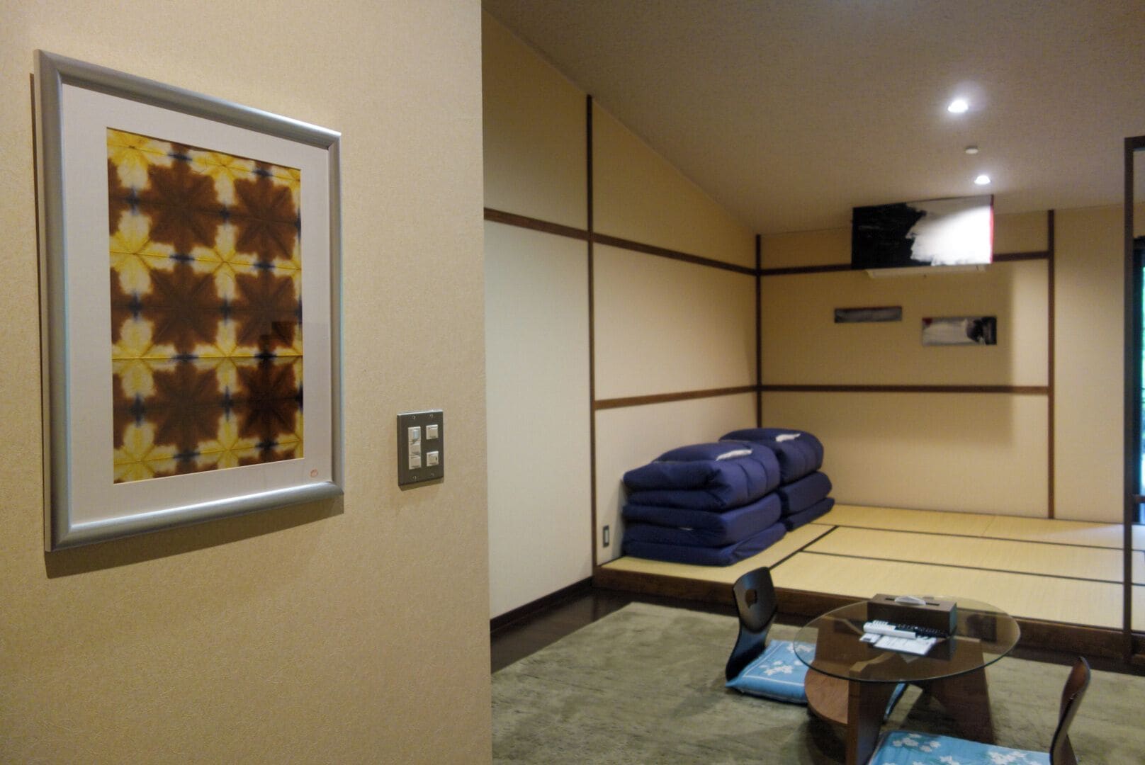 Habitación de hotel con cama, una obra de arte enmarcada en la pared, una mesita con silla, y una pila de equipaje.