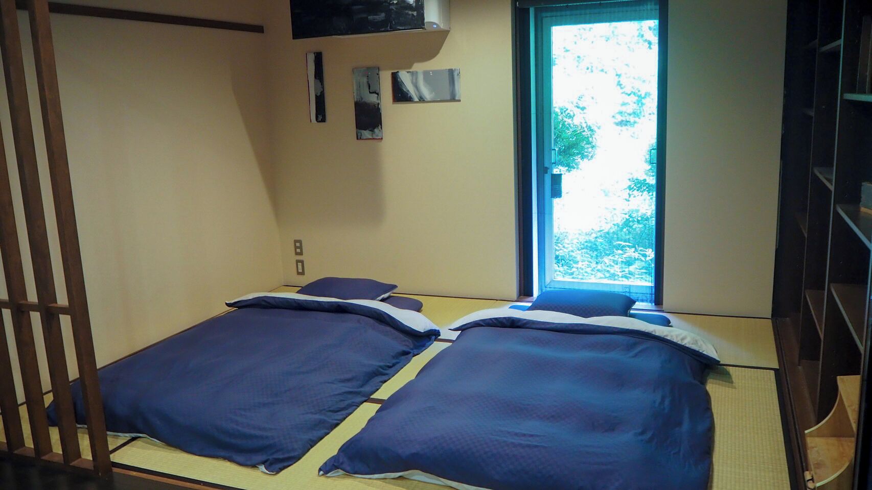 A small room with two beds, a window, and a wooden partition.