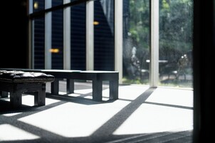 Un banco y una ventana con persianas, dejando que la luz del sol cree diseños en el suelo.